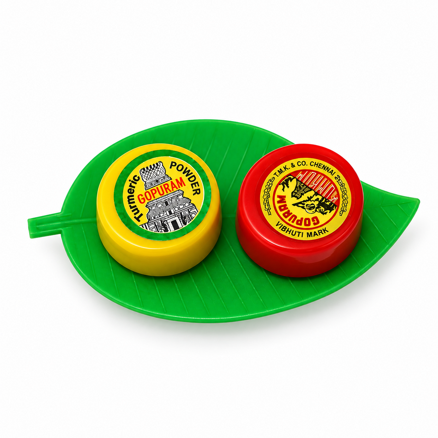 A Gopuram manjal and kumkum set featuring yellow and red containers arranged on a green plastic betel leaf, centered on a solid white background. Available in the UK at theindianshelf.co.uk.