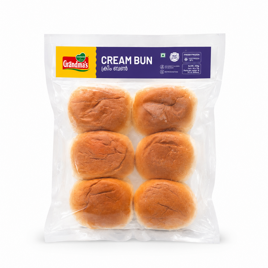 A professional studio product shot of a clear vacuum-sealed transparent pouch containing a pack of six golden-brown Grandma's Fresh Frozen Cream Buns isolated against a pure white background in image_8aec49.jpg. The top of the clear packaging features a distinct yellow and purple header label showing the brand logo, product name, and nutritional highlights. This product is available in the UK at theindianshelf.co.uk.