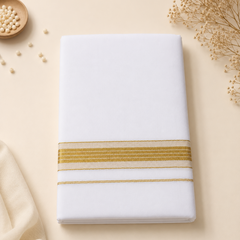 A studio flatlay shot of a neatly folded bright white Kerala Double Mundu on a light cream surface. The cotton fabric features a horizontal border with a thick golden zari band and fine multi-stripe patterns. Delicate dried flowers and a dish of white beads sit in the background. Available in the UK at theindianshelf.co.uk.