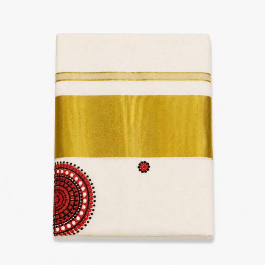 A close-up folded view of an off-white Kerala tissue cotton kasavu set mundu centered on a solid white background, displaying a wide horizontal metallic gold zari band alongside a circular red, black, and white Theyyam crown motif. Available in the UK at theindianshelf.co.uk