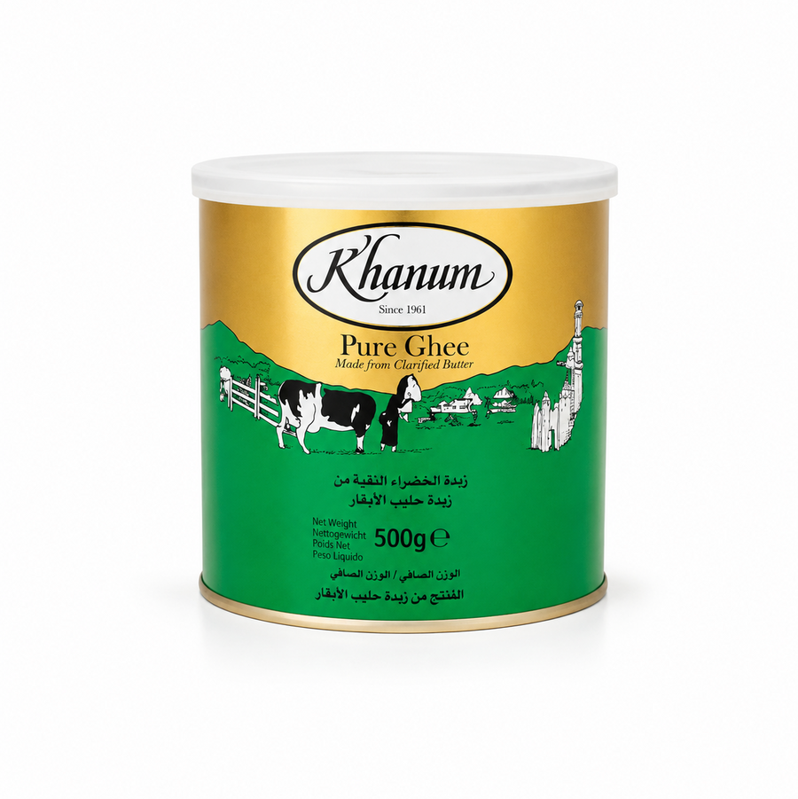 A 500g tin can of Khanum Pure Ghee centered on a solid white background, featuring a gold and green packaging design with the Khanum logo and an illustration of a cow and a traditional figure in a village setting. This product is available in the UK at theindianshelf.co.uk.