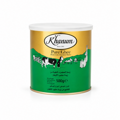 A 500g tin can of Khanum Pure Ghee centered on a solid white background, featuring a gold and green packaging design with the Khanum logo and an illustration of a cow and a traditional figure in a village setting. This product is available in the UK at theindianshelf.co.uk.