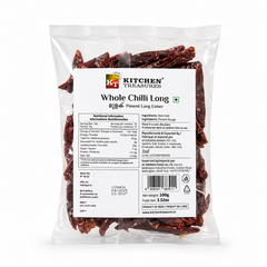 A professional studio product shot of a 100g clear pillow pouch of Kitchen Treasures Whole Chilli Long isolated against a pure white background in image_971bc0.jpg. The transparent packaging clearly showcases the textured, deep crinkled crimson whole red chillies packed inside, centered behind a clean white information label displaying nutritional tables, barcodes, and manufacturing details. This product is available in the UK at theindianshelf.co.uk.