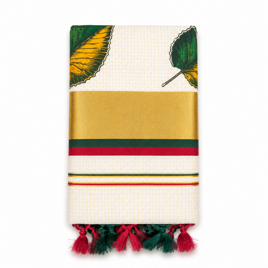 A neatly folded off-white tissue saree centered on a solid white background, featuring fine gold grid check patterns, hand-painted green and yellow leaf motifs, a wide golden kasavu border with green and red accent stripes, and dual-tone red and dark green knotted tassels along the bottom fringe. Available in the UK at theindianshelf.co.uk.