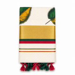 A neatly folded off-white tissue saree centered on a solid white background, featuring fine gold grid check patterns, hand-painted green and yellow leaf motifs, a wide golden kasavu border with green and red accent stripes, and dual-tone red and dark green knotted tassels along the bottom fringe. Available in the UK at theindianshelf.co.uk.