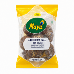 A professional studio product shot of a transparent plastic pillow pouch packed with large, dark golden-brown spherical Mayil Jaggery Balls against a solid white background. The packaging features a bright yellow border along both the top and bottom sections. In the upper center, a large oval green logo displays the brand name "Mayil" in yellow with a stylized peacock feather icon. This product is available in the UK at theindianshelf.co.uk.