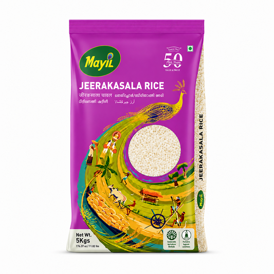 A professional studio product shot of a rectangular 5kg bag of Mayil Jeerakasala Rice standing vertically against a solid white background. The front of the packaging features a vibrant magenta background on the upper portion, showcasing the oval green "Mayil" logo on the left and a white "50 Plus Years" heritage badge on the right. Below the bold white title "JEERAKASALA RICE", a magnificent illustration of a golden peacock spreads its long,This product is available in the UK at theindianshelf.co.uk.
