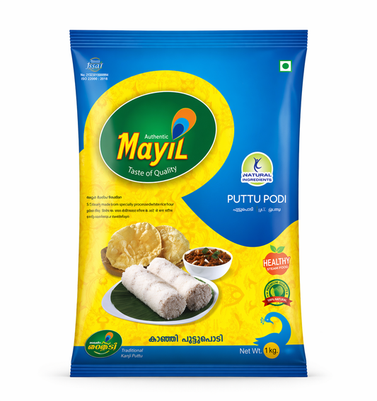 A high-quality studio shot of a 1kg packet of Mayil Puttu Podi. The packaging features a vibrant blue and yellow design with a large green oval containing the "Mayil" peacock logo. accompanied by a small white bowl of curry and golden papadums. Several quality seals, including "Natural Ingredients," "Healthy Steam Food," and "100% Natural," are clearly visible. The net weight is marked as 1 kg . this product is available in the UK at theindianshelf.co.uk.