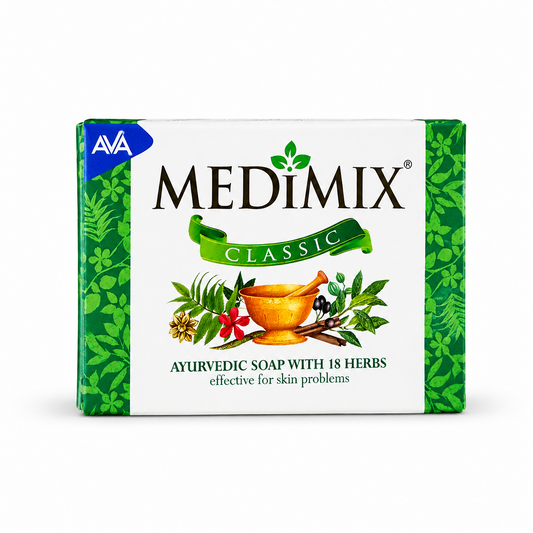 Studio product shot of a rectangular bar of Medimix Classic Ayurvedic Soap packaging against a plain white background. The paper wrapper has a broad white central body flanked by bright green borders decorated with an elegant leaf-and-flower pattern. The top left features a sharp blue triangle containing the white "AVA" brand crest. The bold black name "MEDIMIX" This product is available in the UK at theindianshelf.co.uk.