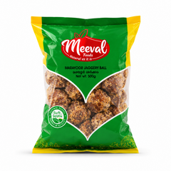 A professional studio product shot of a 500g pouch of Meeval Foods Marayoor Jaggery Ball isolated against a pure white background in image_81efe0.jpg. The green, yellow, and red packaging includes a large, clear V-shaped window showing the rustic brown jaggery balls inside.