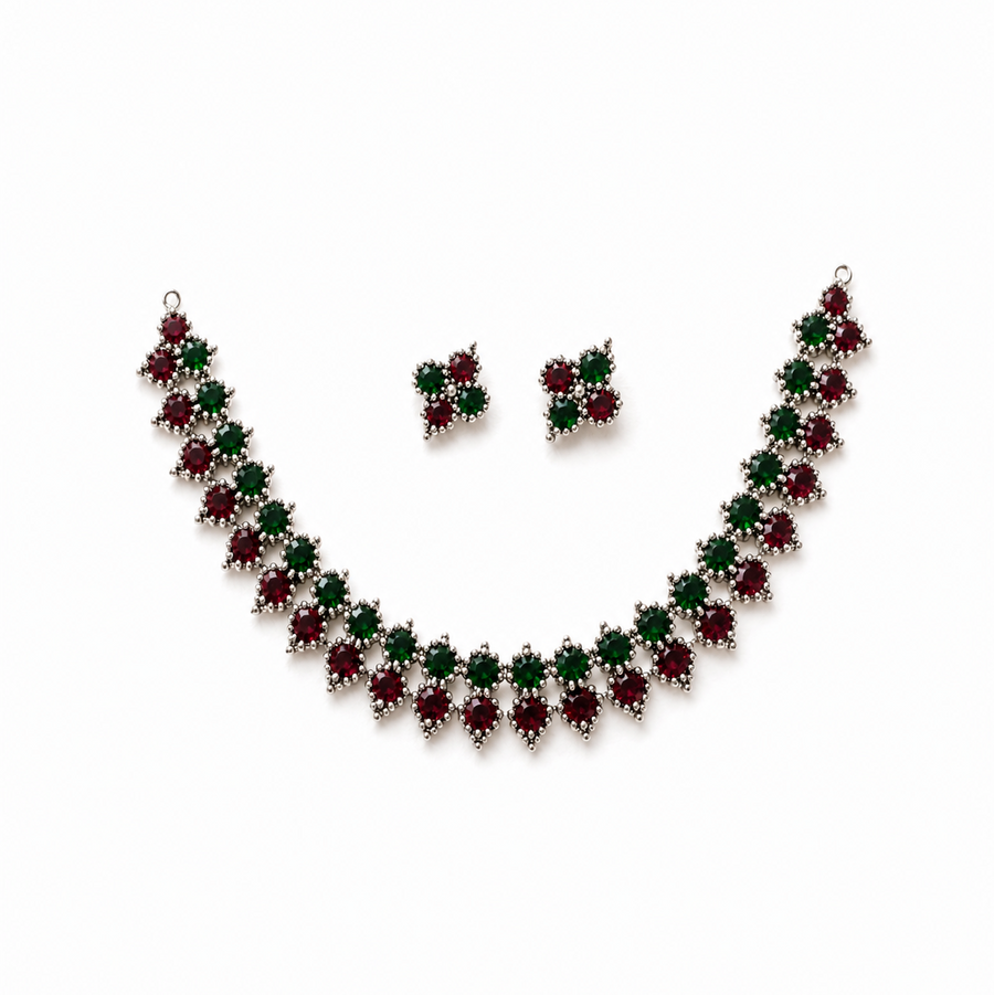 A studio product shot of an antique oxidized silver Choker Necklace and Earrings Set isolated on a white background. The jewelry features a zigzag pattern of red and green stones. Available in the UK at theindianshelf.co.uk.