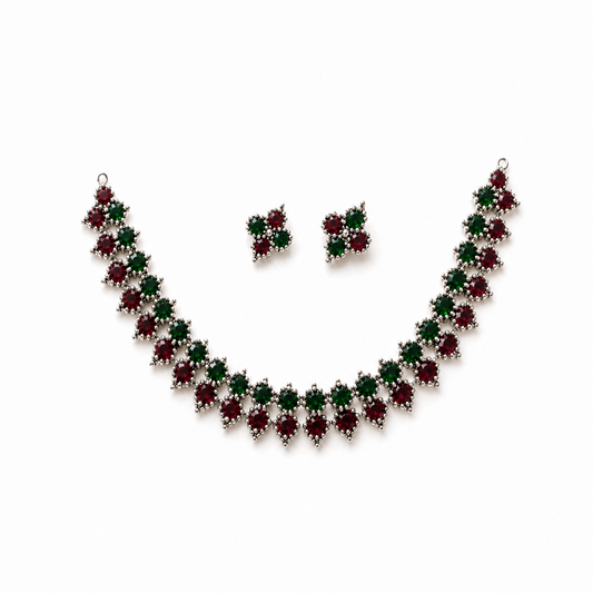 A studio product shot of an antique oxidized silver Choker Necklace and Earrings Set isolated on a white background. The jewelry features a zigzag pattern of red and green stones. Available in the UK at theindianshelf.co.uk.