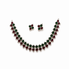 A studio product shot of an antique oxidized silver Choker Necklace and Earrings Set isolated on a white background. The jewelry features a zigzag pattern of red and green stones. Available in the UK at theindianshelf.co.uk.