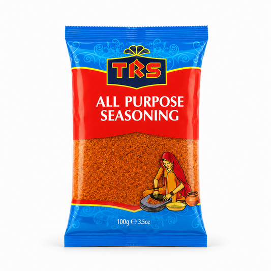 A 100g pouch of TRS All Purpose Seasoning centered on a solid white background, featuring a vibrant blue and red packaging design with the TRS logo and a clear window showing the orange-brown grounded spice mix next to an illustration of a woman using a grinding stone. This product is available in the UK at theindianshelf.co.uk.