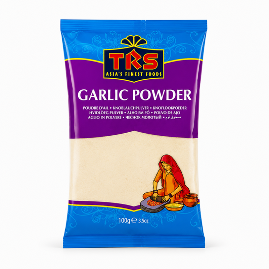 A 100g pouch of TRS Garlic Powder centered on a solid white background, featuring a vibrant purple and blue packaging design with the TRS logo and a clear window showing off-white finely ground garlic powder next to an illustration of a traditional Indian woman using a grinding stone. This product is available in the UK at theindianshelf.co.uk.