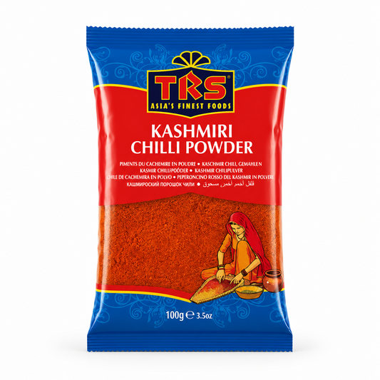 A 100g pouch of TRS Kashmiri Chilli Powder centered on a solid white background, featuring a vibrant red and blue packaging design with the TRS logo and a clear window showing rich, finely ground red chilli powder next to an illustration of a traditional Indian woman. This product is available in the UK at theindianshelf.co.uk.