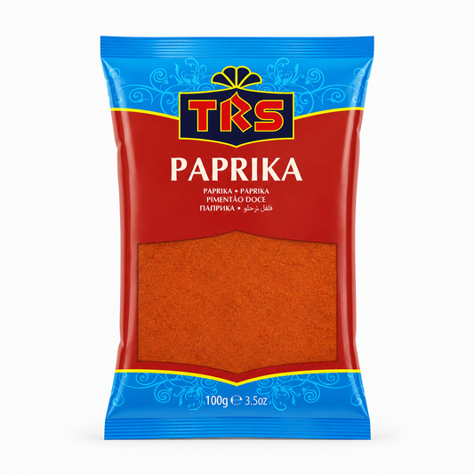 A 100g pouch of TRS Paprika centered on a solid white background, featuring a bright red and blue packaging design with the TRS logo and a clear window displaying finely ground red paprika powder. This product is available in the UK at theindianshelf.co.uk.