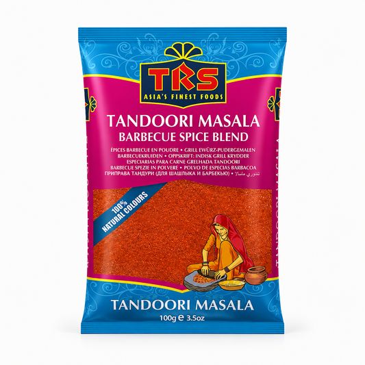 A 100g pouch of TRS Tandoori Masala Barbecue Spice Blend centered on a white background, featuring a vibrant blue and magenta label with the brand logo and an illustration of a woman traditional-grinding spices, displaying the bright red spice blend through a transparent lower window. This product is available in the UK at theindianshelf.co.uk.