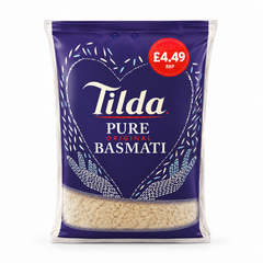 A bag of Tilda Pure Original Basmati Rice centered on a solid white background, featuring a deep blue package with a white heart design formed by rice grains, a red £4.49 RRP price flash, and a transparent lower window displaying the long raw rice grains. This product is available in the UK at theindianshelf.co.uk.