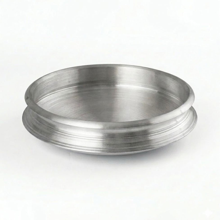 A clean, eye-level studio shot of a traditional Aluminum Uruli (cookware). The vessel is circular with a wide, open top and a shallow depth, featuring a distinctive flared rim with horizontal decorative grooves. It has a brushed metallic finish and is set against a plain, well-lit white background.