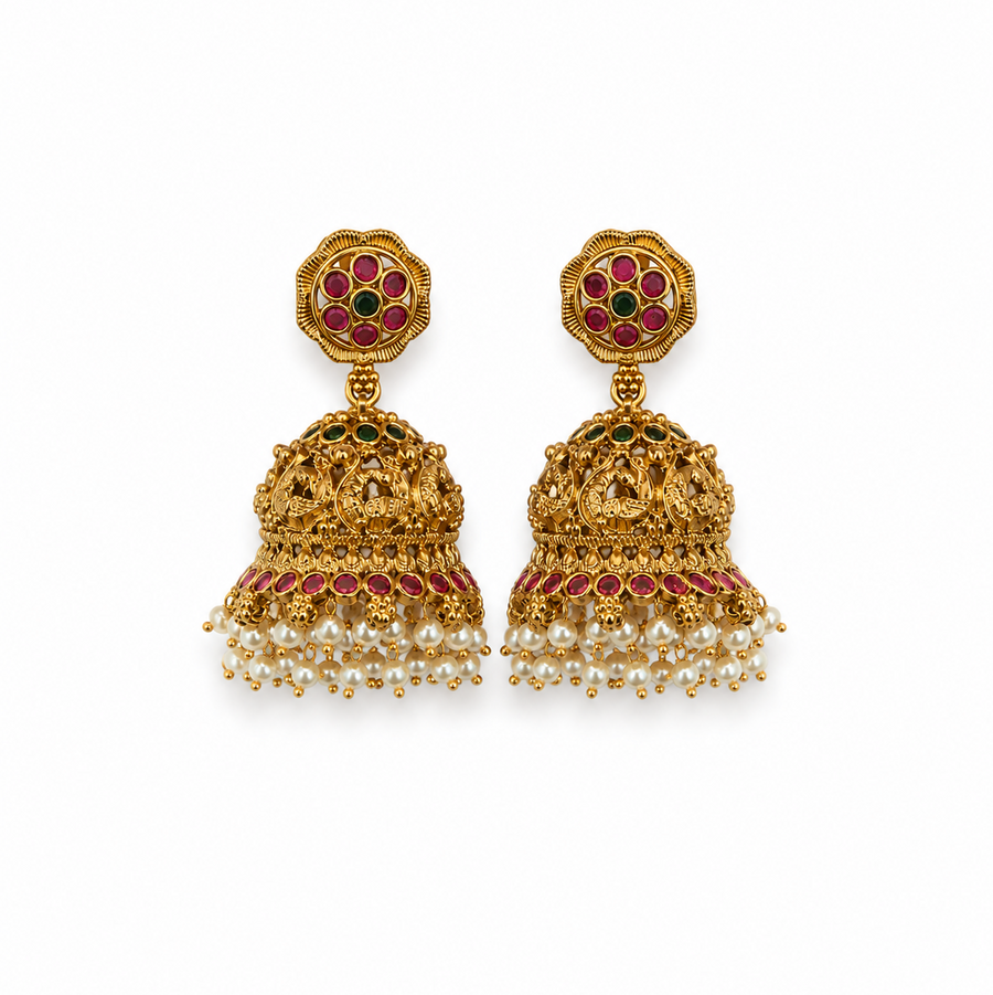 A pair of antique gold-toned temple jhumka earrings featuring floral studs, ruby and emerald stone accents, and a fringe of white pearl drops, centered against a solid white background. Available in the UK at theindianshelf.co.uk.