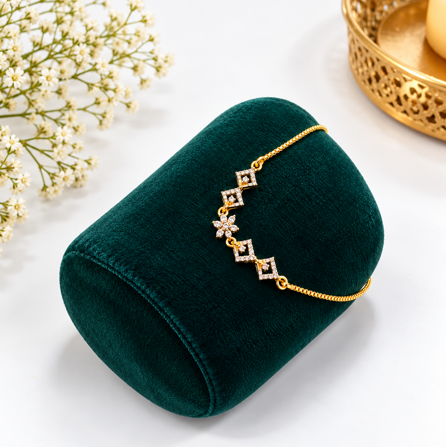 A delicate gold-finish adjustable chain bracelet with cubic zirconia floral and geometric charms displayed on an emerald green velvet cushion. Available in the UK at theindianshelf.co.uk.