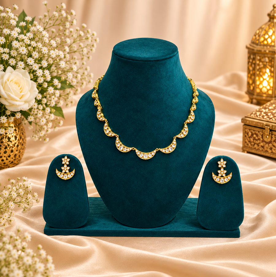 A gold-plated crescent moon American diamond necklace and matching earring set displayed on a deep teal velvet bust against a warm, decorative background. Available in the UK at theindianshelf.co.uk.