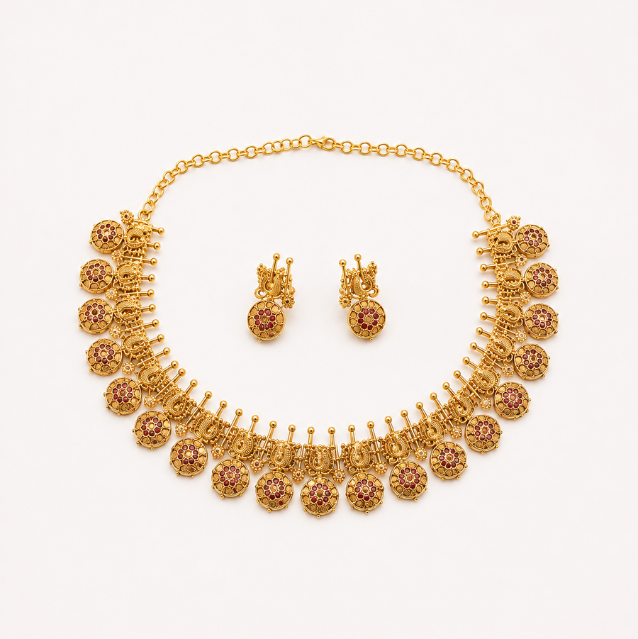 An antique gold-plated heritage jewelry set featuring a traditional peacock choker necklace adorned with ruby red stone circular drops and matching drop earrings, centered on a solid white background. Available in the UK at theindianshelf.co.uk.