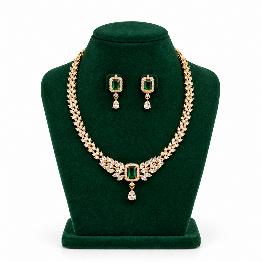 A gold-plated necklace set featuring emerald-green central stones and sparkling white CZ leaf patterns,displayed on a green velvet bust. Available in the UK at theindianshelf.co.uk.
