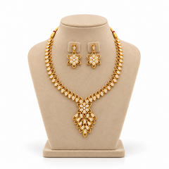 A gold-plated necklace set featuring an elaborate floral leaf cluster pendant encrusted with white CZ stones, displayed on a beige velvet mannequin bust. Available in the UK at theindianshelf.co.uk.
