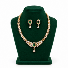 A gold-plated necklace set featuring emerald-green central stones and sparkling white CZ leaf patterns,displayed on a green velvet bust. Available in the UK at theindianshelf.co.uk.