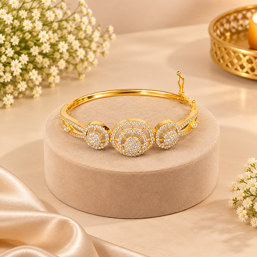 A high-shine gold openable bangle featuring three concentric circular wheel motifs set with brilliant white cubic zirconia stones, displayed on a velvet podium. Available in the UK at theindianshelf.co.uk.