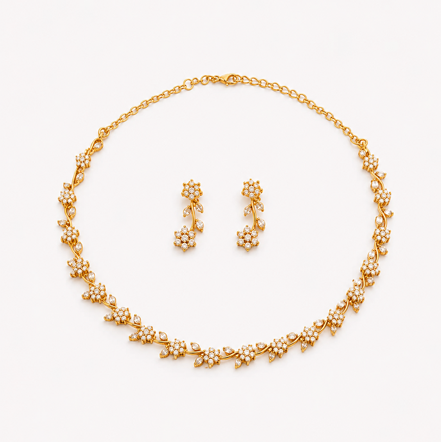 A coordinated matte gold-plated jewelry set featuring a delicate floral vine collar necklace and matching drop earrings encrusted with sparkling clear American Diamond (AD) stones, centered on a solid white background. Available in the UK at theindianshelf.co.uk.
