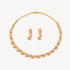 A coordinated matte gold-plated jewelry set featuring a delicate floral vine collar necklace and matching drop earrings encrusted with sparkling clear American Diamond (AD) stones, centered on a solid white background. Available in the UK at theindianshelf.co.uk.