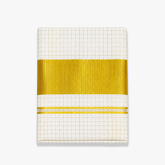 A close-up folded view of an off-white Kerala tissue cotton kasavu single set mundu centered on a solid white background, displaying an all-over golden check grid pattern and a wide horizontal metallic gold zari border with fine accent lines. Available in the UK at theindianshelf.co.uk.