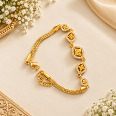 A polished gold-finish designer bracelet featuring geometric diamond-shaped stations encrusted with white stones and a textured mesh chain, displayed on a neutral background. Available in the UK at theindianshelf.co.uk.