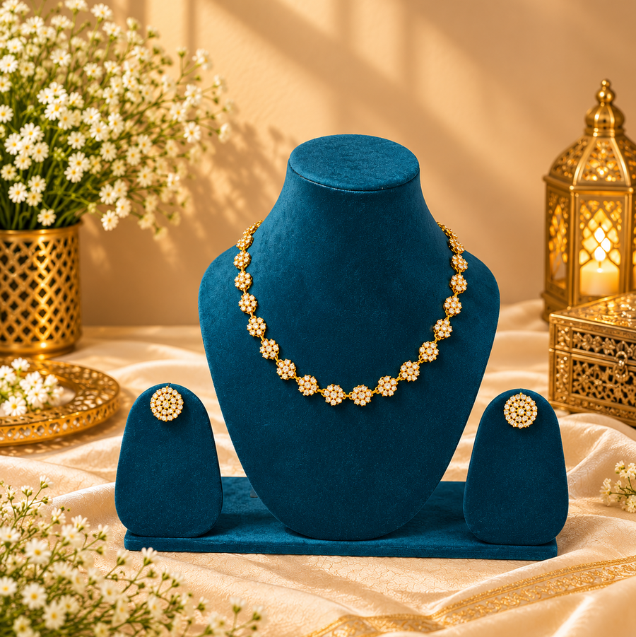 A polished gold-tone necklace and earring set featuring linked floral stations encrusted with sparkling white American diamonds, displayed on teal velvet stands. Available in the UK at theindianshelf.co.uk.